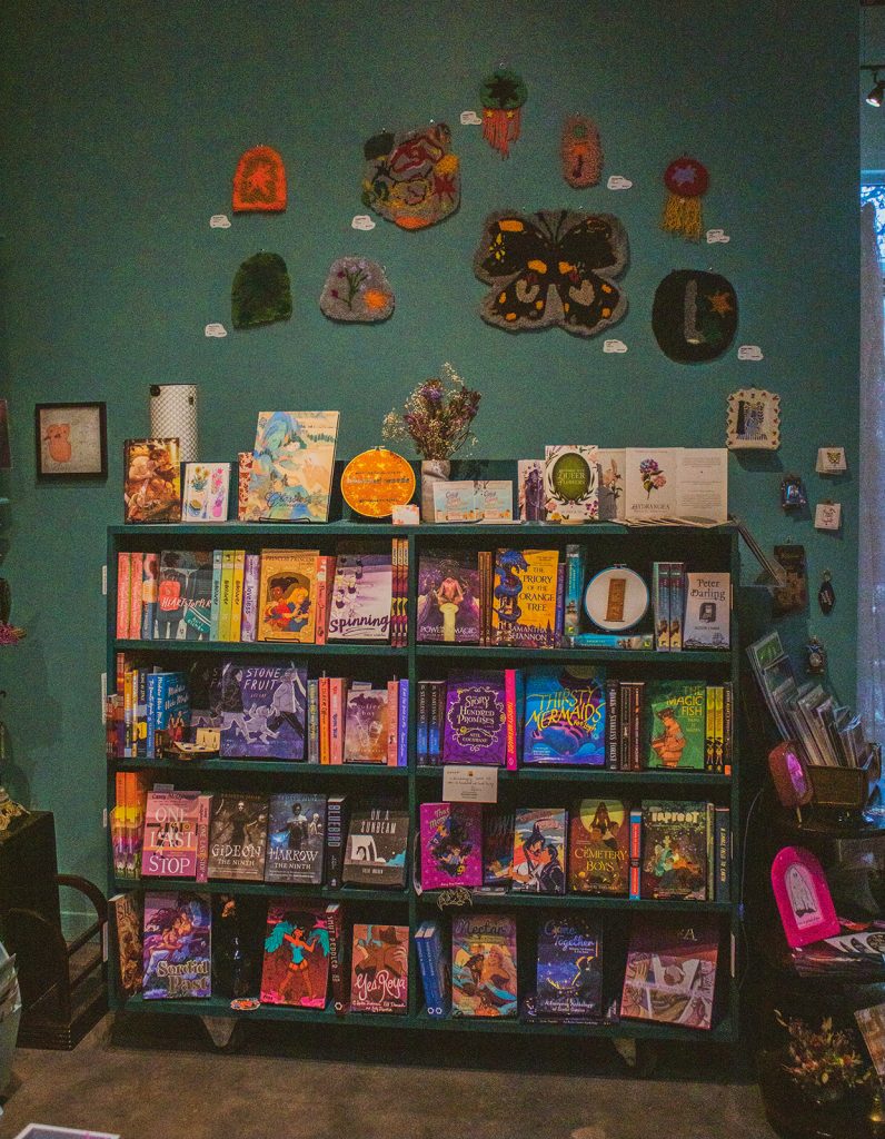 A bookshelf display mostly featuring assorted comics, surrounded by zines with some felt patches on the wall above.